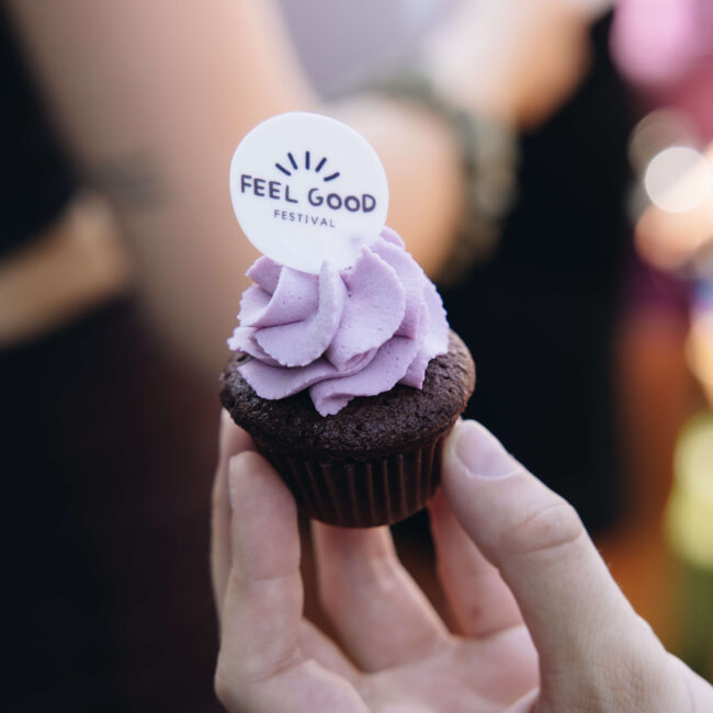 Hand hält einen Cupcake mit lila Creme und Topper des Feel Good Festival