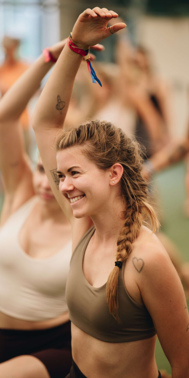 Lächelnde Frau streckt den Arm bei einer Fitnessübung inmitten der Gruppe