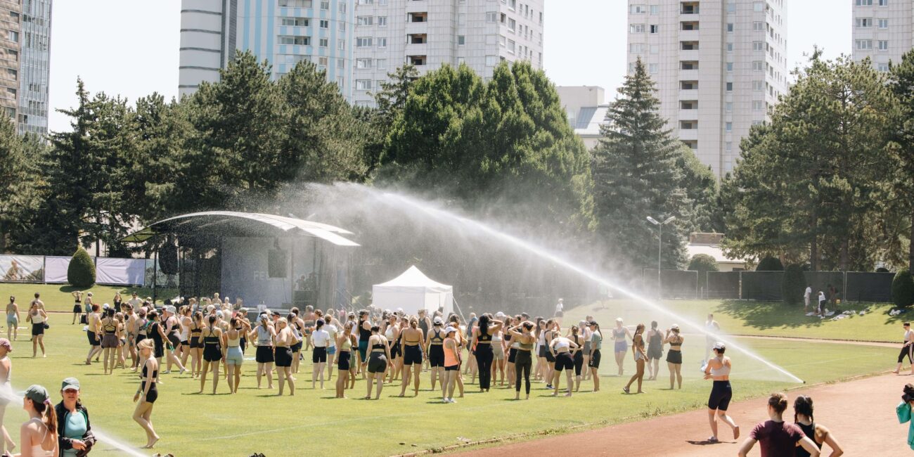 Gruppe wird von mehreren Wasserfontänen auf dem Sportplatz abgekühlt