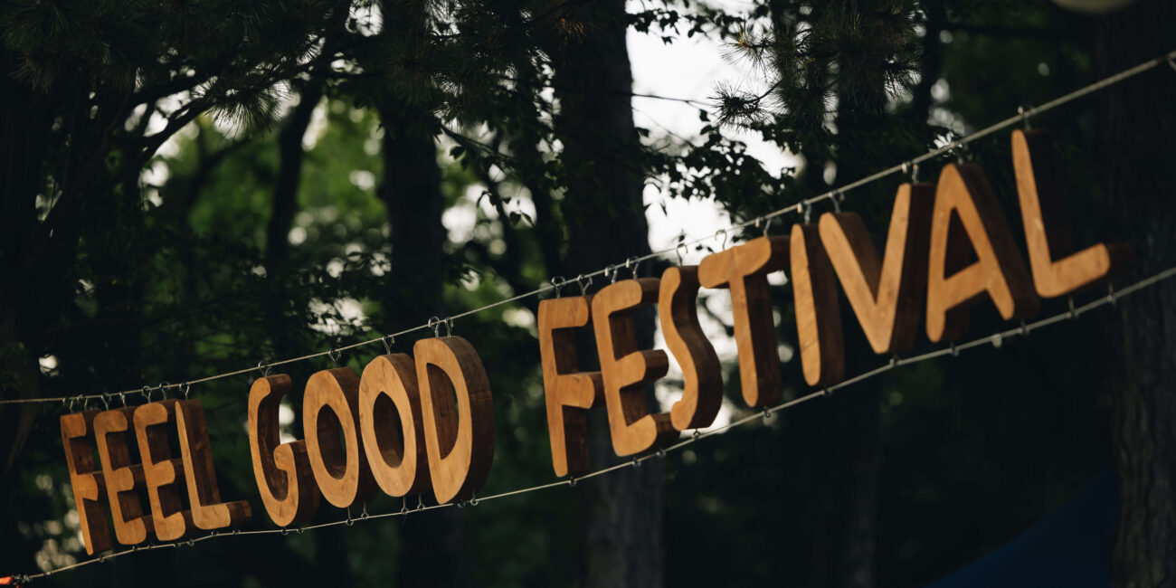 Holzschriftzug 'Feel Good Festival' hängt zwischen Bäumen auf dem Festivalgelände