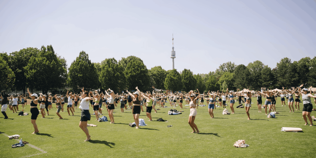 Große Gruppe tanzt synchron mit erhobenen Armen auf der Festivalwiese, im Hintergrund der Donauturm
