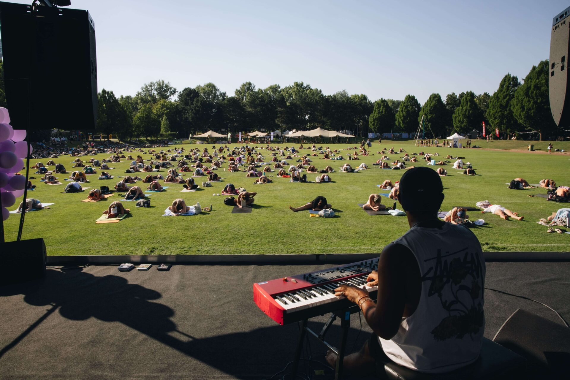 Musiker spielt Keyboard auf der Bühne, davor liegt die Gruppe entspannt auf der Wiese
