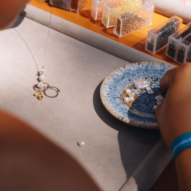 Person fertigt an einem Marktstand ein Perlenarmband, Bastelstation beim Feel Good Festival